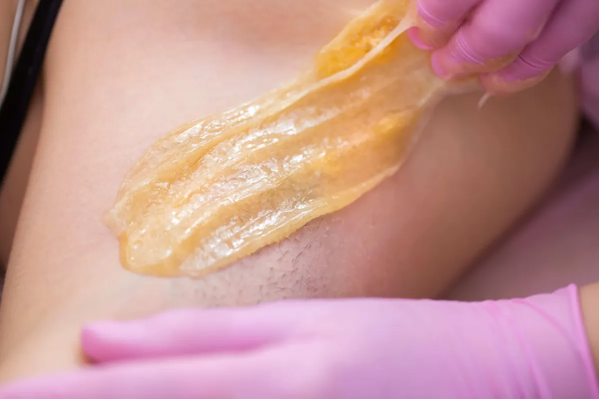 Aesthetician spreading wax on a person's leg preparing for a Brazilian wax